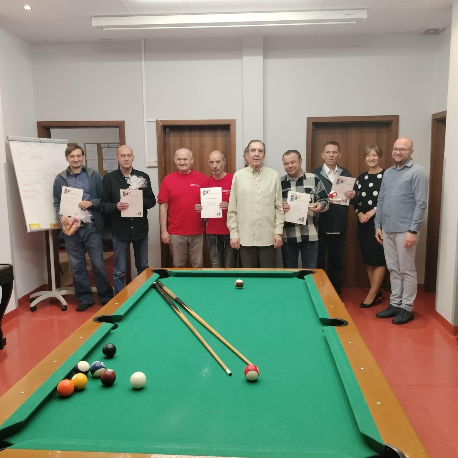 Grupa ludzi z dyplomami pozująca do zdjęcia. Na pierwszym planie stół bilardowy. 