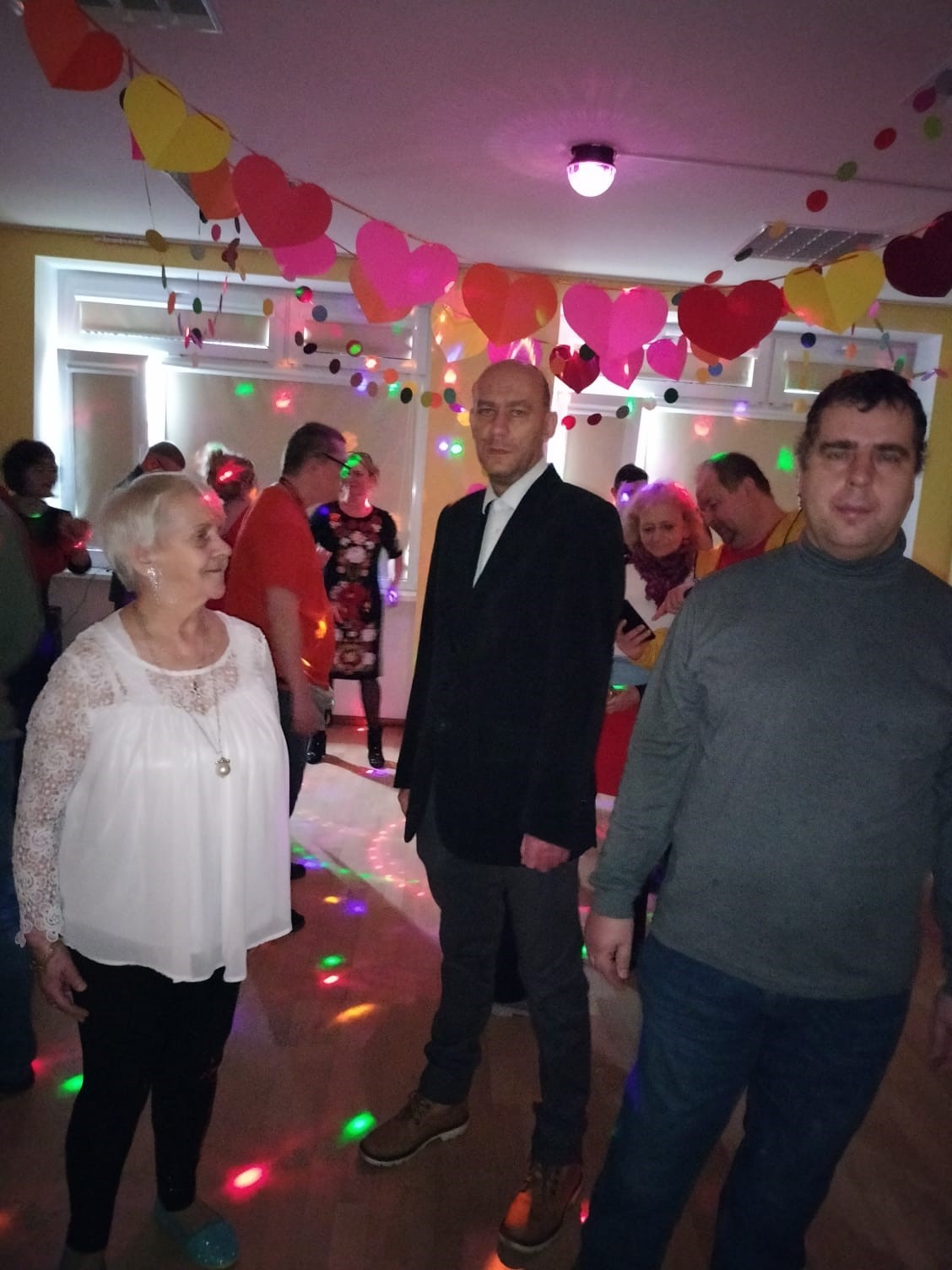 Grupa osób na parkiecie tanecznym. W tle dekoracja walentynkowa. 
