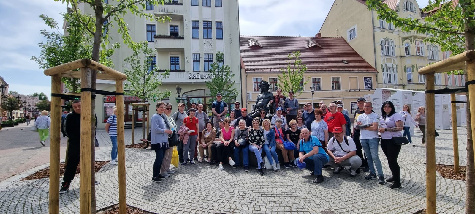 Grupa osób pozująca do zdjęcia na moście. W tle panorama miasta. 