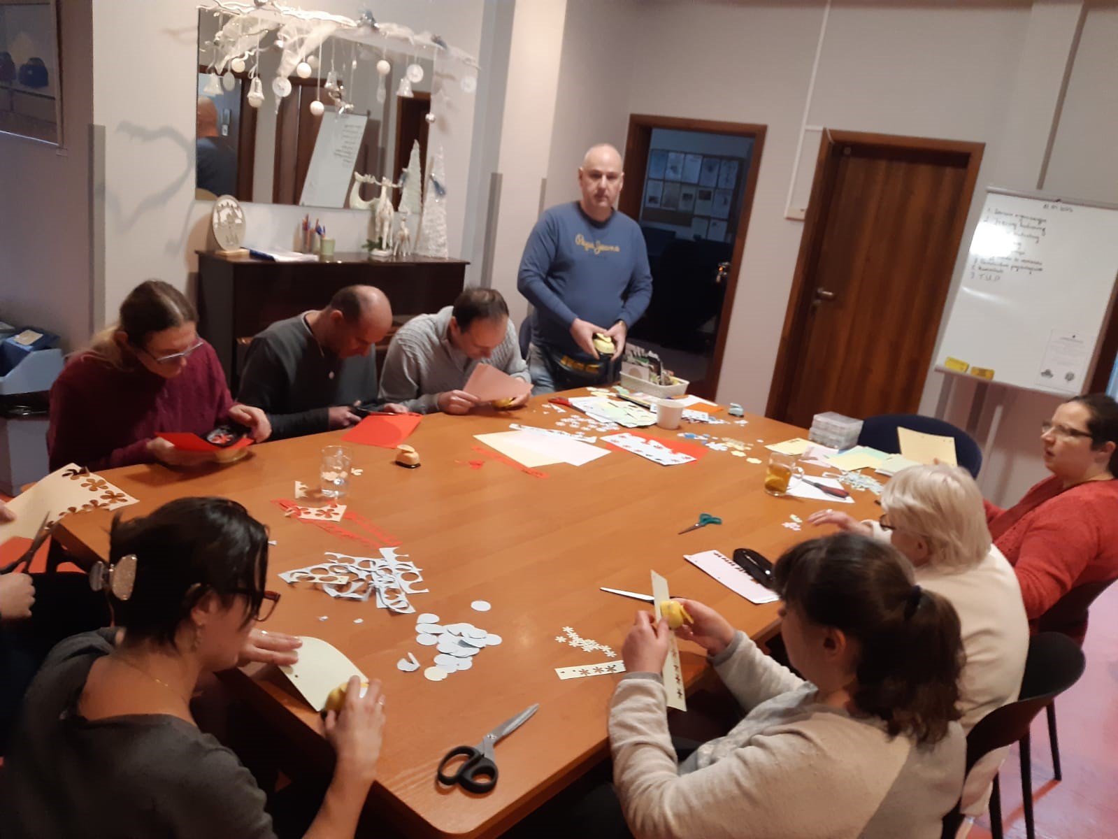 Grupa kobiet i mężczyzn zgromadzona przy stole podczas zajęć manualnych. 