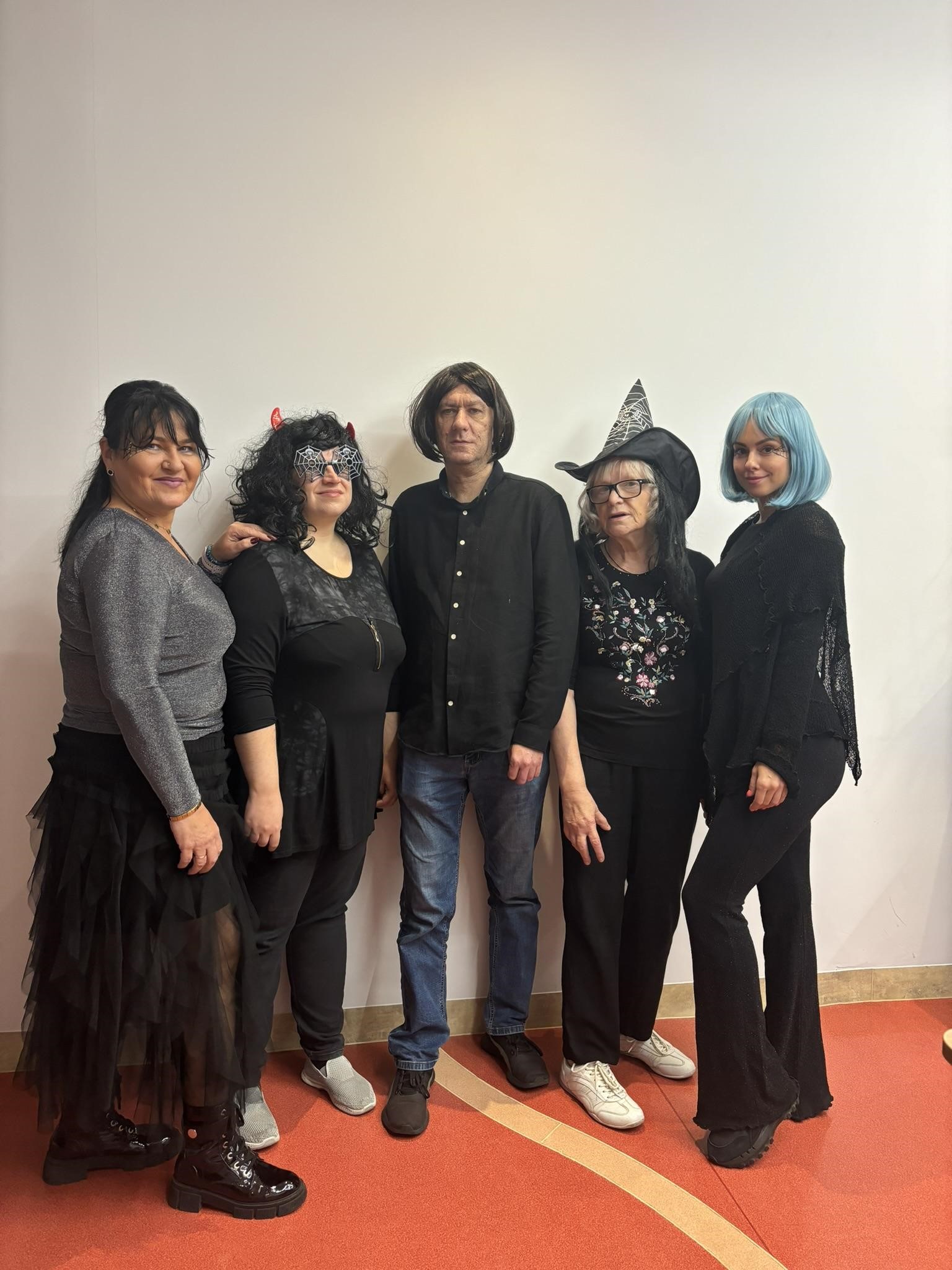 Cztery kobiety i jeden mężczyzna pozujący w strojach halloweenowych. W tle widać białą ścianę.