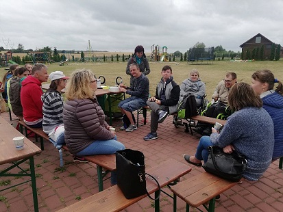 Grupa uczestników wraz z terapeutami siedzi na ławkach., które są ustawione w krąg. 