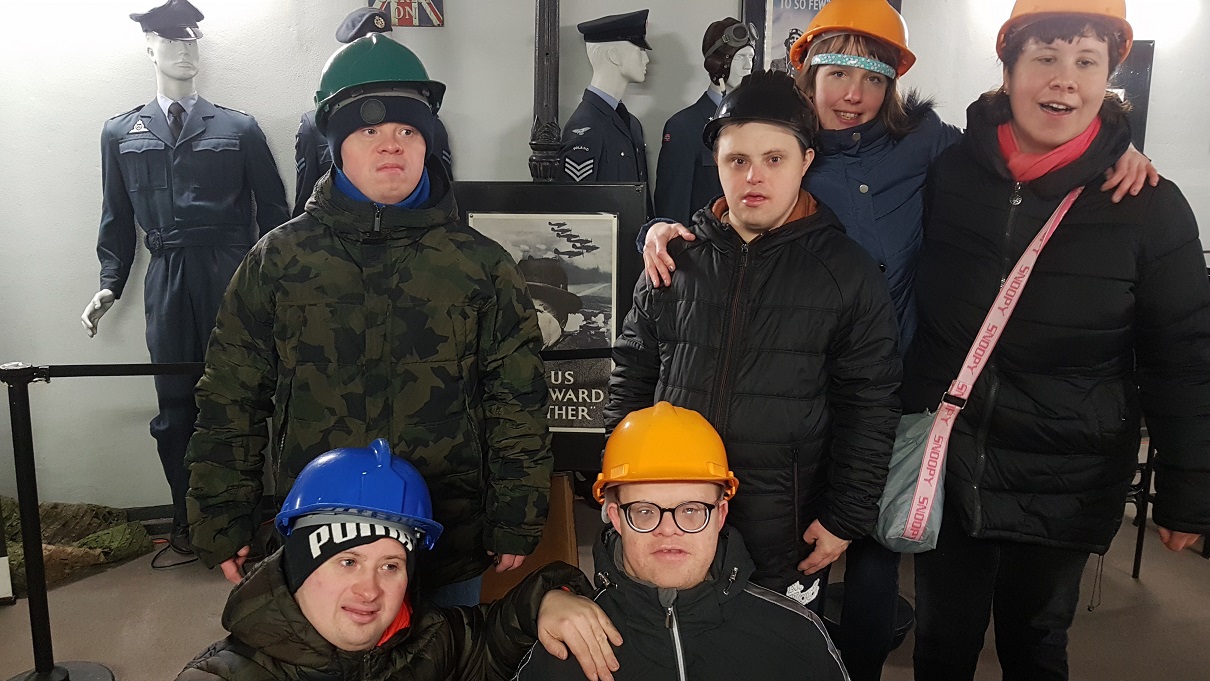 Grupa 6 uczestników stoi obok siebie. Na głowach mają kaski ochronne. Za nimi znajdują się plastikowe manekiny ubrane w mundury. 