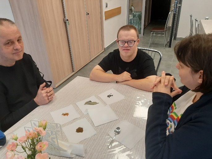 Trzy osoby przyszywające guziki do fragmentu tkaniny.