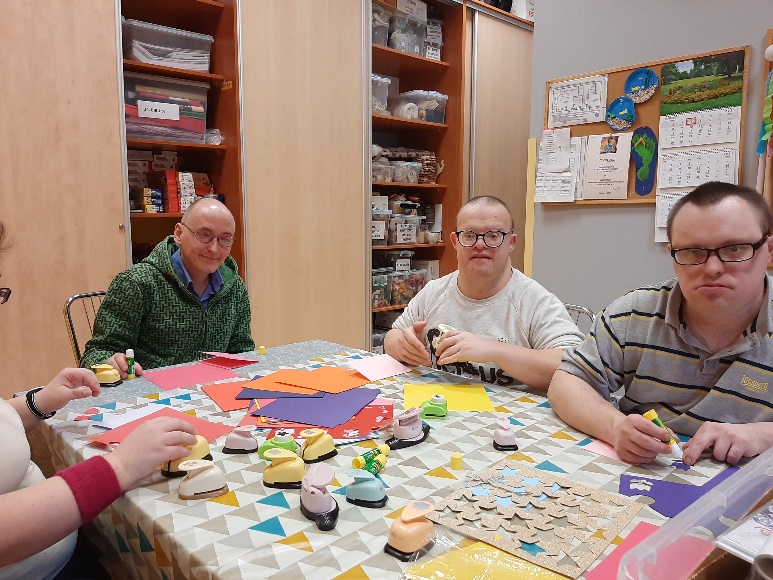  Trzech mężczyzn  siedzących przy stole, na którym znajdują się materiały plastyczne.