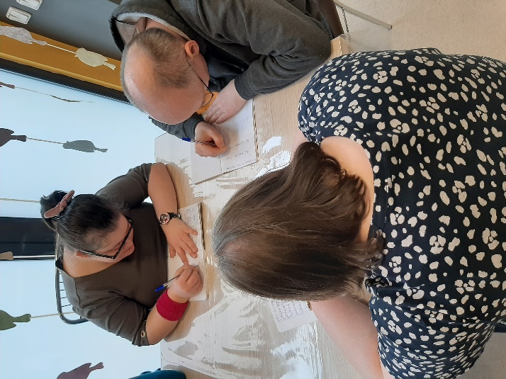 Trzy osoby siedzące i piszące przy stole.