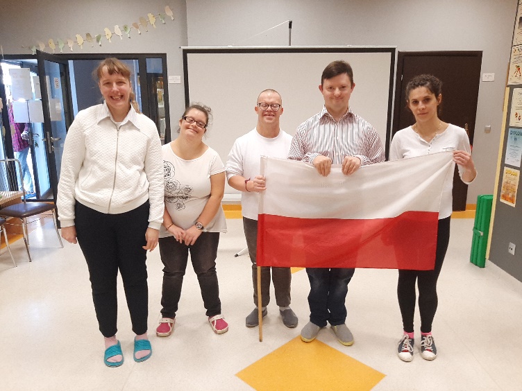 Grupa uczestników, ubranych na galowo trzymających w dłoni flagę biało-czerwoną.