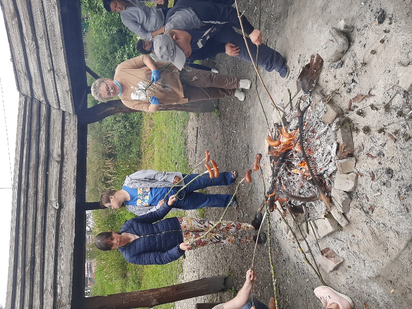 Grupa osób piekących kiełbaski na ognisku.     