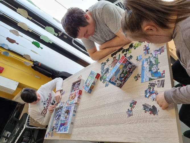Przy stole siedzi dwóch mężczyzn i kobieta. Każdy z nich układa puzzle.