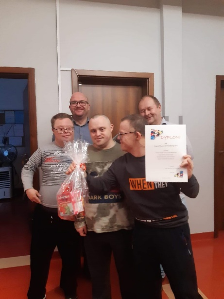 Mężczyźni stoją. Jeden z nich trzyma dyplom i nagrodę.