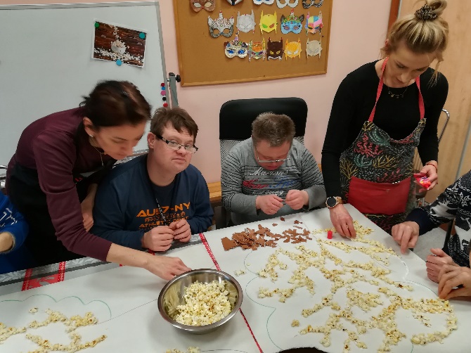 Kobiety i mężczyźni siedzą przy stole i robią pracę plastyczną.