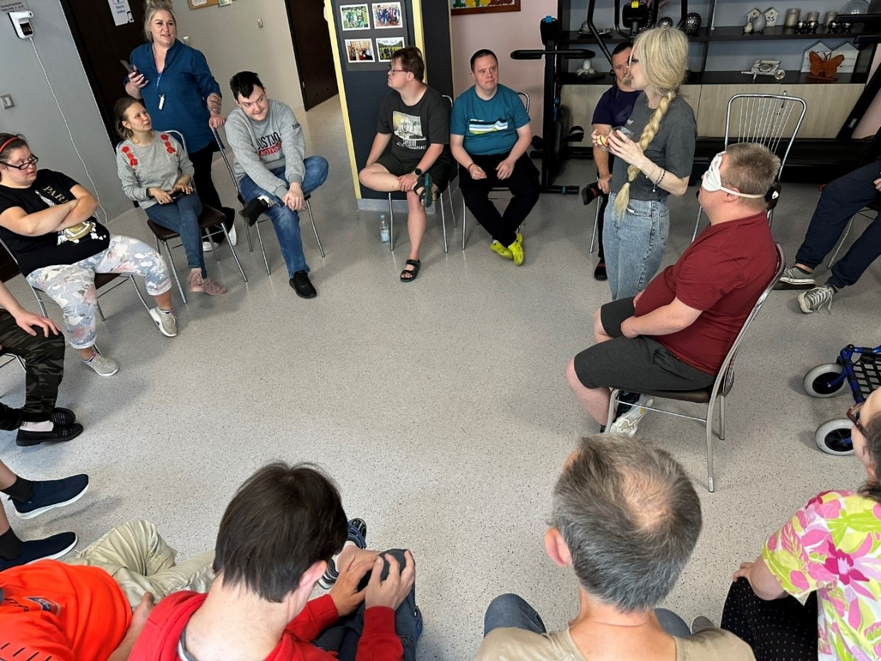 Grupa kobiet i mężczyzn siedzi na krzesłach w kole.