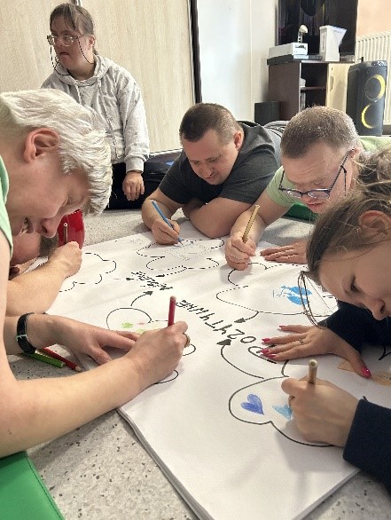 Grupa Uczestników przygotowuje wspólny plakat z okazji Dnia Pozytywnego Myślenia.