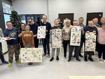 Grupa mężczyzn i kobiet trzymają wykonane prace.