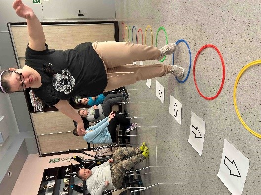 Kobieta stojąca na jednej nodze w kolorowym kole ułożonym na podłodze.