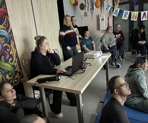 Grupa kobiet i mężczyzn oglądająca wyświetlone na ekranie zdjęcia.