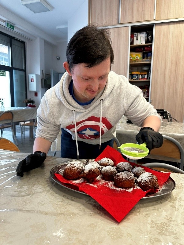 Mężczyzna posypuje pączki cukrem pudrem przez małe sitko.