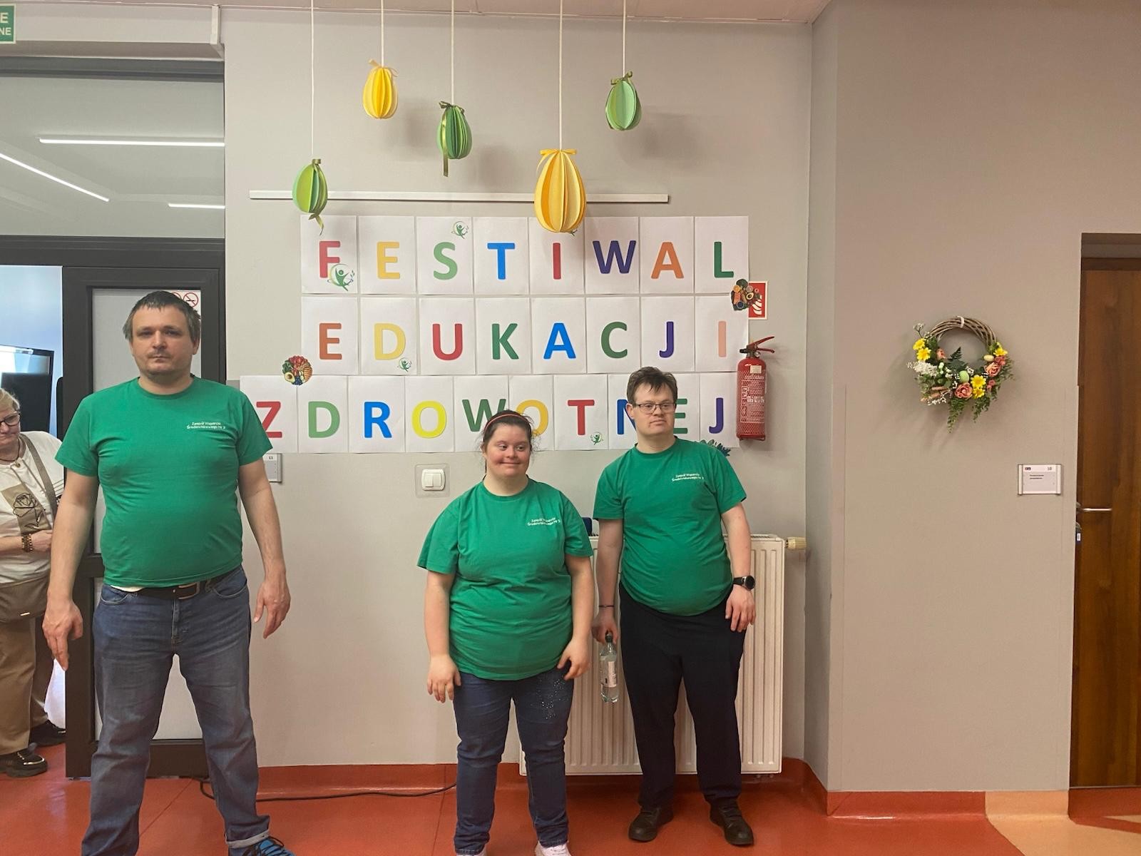 Grupa trzech osób w zielonych koszulkach pozuje do zdjęcia. Patrzą prosto w obiektyw. 